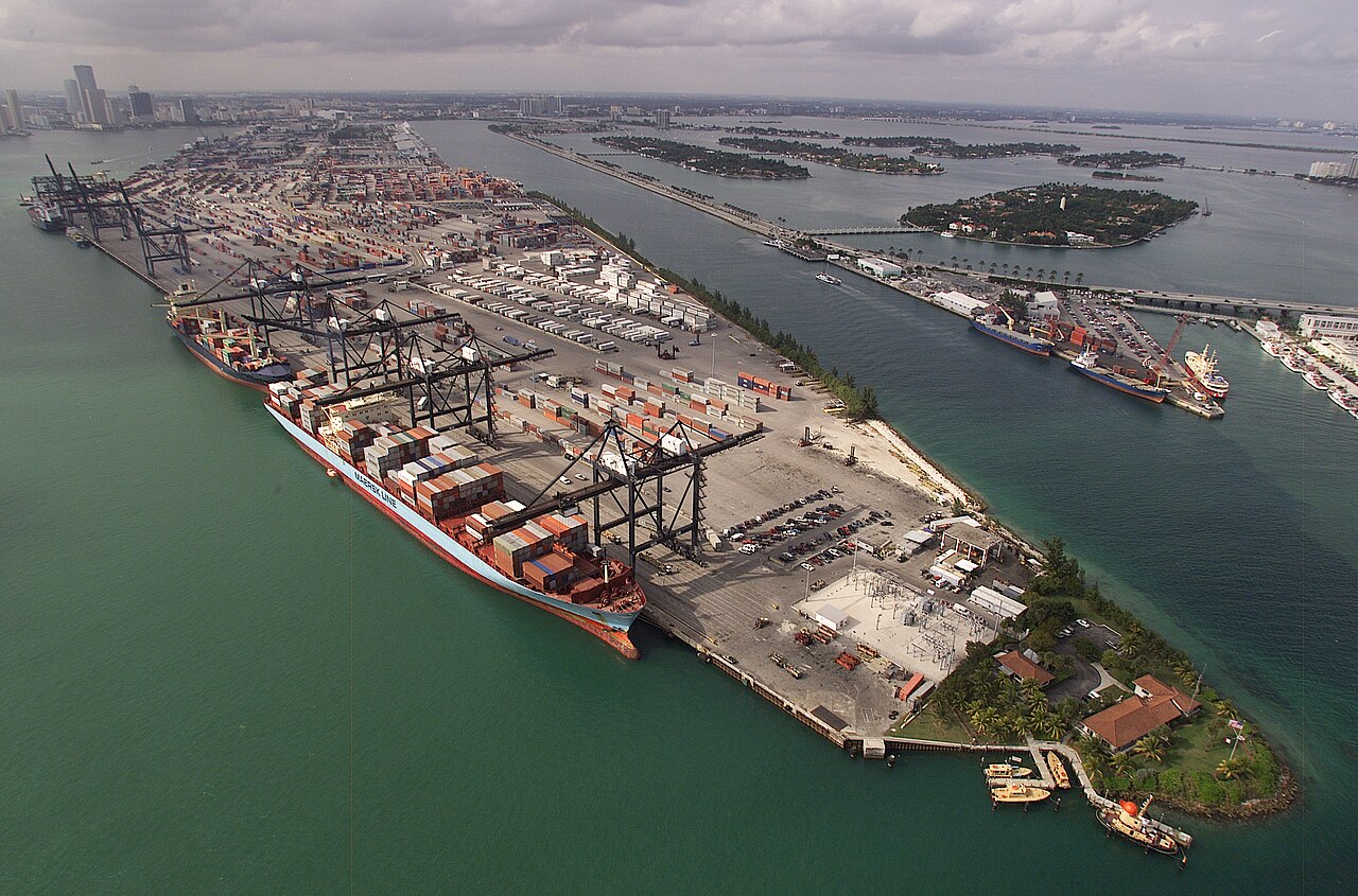 Container cranes and cargo ships along PortMiami, with Miami’s skyline and surrounding islands in the distance